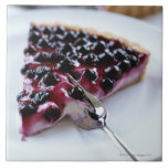 Fork slicing blueberry pie on plate ceramic tile