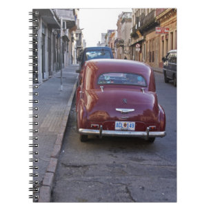 A classic old red Peugeot car parked on a street Notebook
