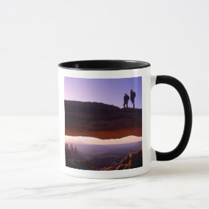 A couple watches sunrise from atop Mesa Arch in Mug