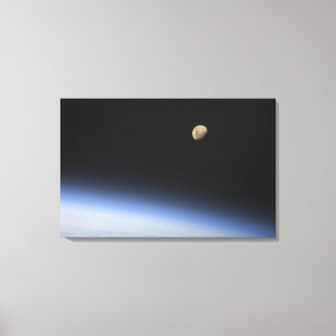 A gibbous moon visible above Earth's atmosphere Canvas Print