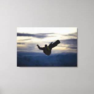 A male snowboarder does a back flip while riding canvas print
