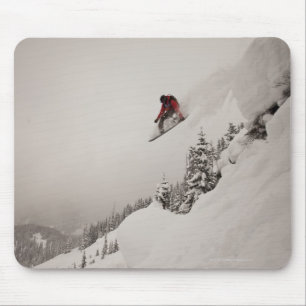 A snowboarder jumps off a cliff into powder in mouse pad