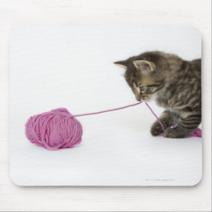 A young tabby kitten playing with a ball of mouse pad