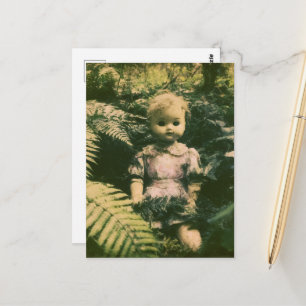 An abandoned spooky doll in the forest postcard