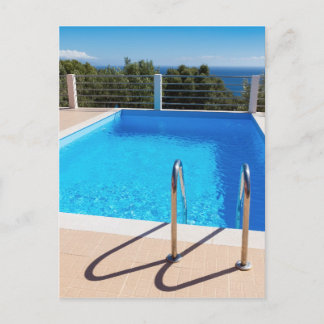 Blue swimming pool with steps at sea postcard