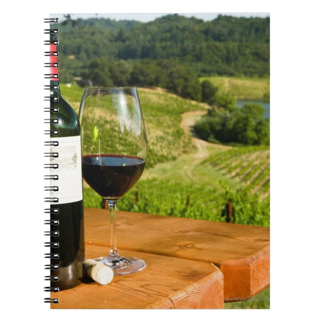 Bottle of red wine and glass on table spiral notebook (Front)