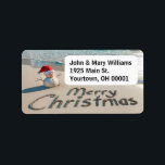 Christmas Sand Man On a Beach Label<br><div class="desc">A small sand snowman wearing a Santa hat stands on an ocean beach with "Merry Christmas" written in the sand.
Text can be changed.</div>