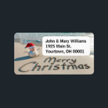 Christmas Sand Man On a Beach Label<br><div class="desc">A small sand snowman wearing a Santa hat stands on an ocean beach with "Merry Christmas" written in the sand.
Text can be changed.</div>
