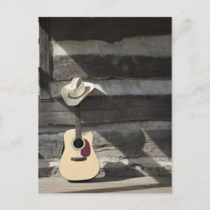 Cowboy hat on guitar leaning on log cabin postcard
