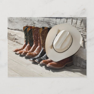 Cowboy hat on row of cowboy boots outside a log postcard