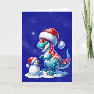 Dinosaur with santa hat building a snowman holiday card
