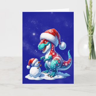 Dinosaur with santa hat building a snowman holiday card