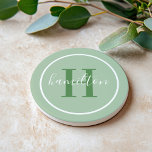 Elegant Sage Green Round Monogram Script Coaster<br><div class="desc">An elegant sandstone coaster featuring a leafy green serif initial and custom family name in script, framed by a white circle on a soft sage green background. The earthy, organic tones bring a calming, botanical warmth to any space. A beautiful personalised gift for housewarmings, garden lovers, or nature-inspired decor. All...</div>