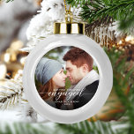 First Christmas Engaged Photo Modern White Script<br><div class="desc">Commemorate your engagement with this beautiful modern keepsake ornament. The white text reads "Our first Christmas engaged, " with the word "engaged" in elegant calligraphy script with decorative swashes before and after. Replace the sample image with your favourite photo, and add your names and the year. A dark gradient filter...</div>