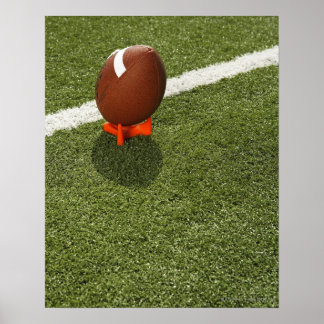 Football atop tee on football field, elevated poster