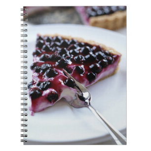 Fork slicing blueberry pie on plate spiral notebook