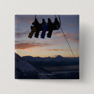 Four snowboarders are silhouetted on a ski lift 15 cm square badge