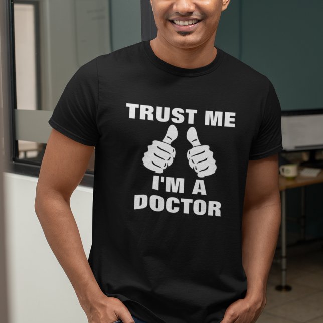 Funny Trust Me I'm a Doctor T-Shirt (Man wearing a black "Trust Me, I'm A Doctor" t-shirt with thumbs-up graphic.)