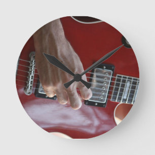 Hand playing red electric guitar near pickup round clock