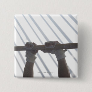 Hands of a male gymnast gripping a horizontal 15 cm square badge