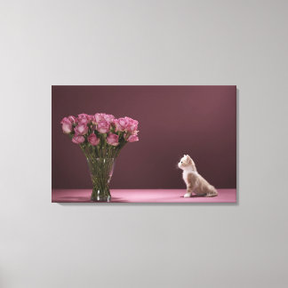 Kitten looking at vase of roses canvas print