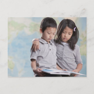 Korean children reading book near map postcard