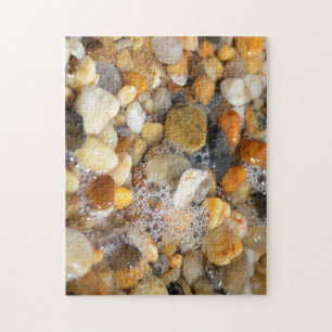 Lots of tumbled rocks on a sandy beach with water  jigsaw puzzle