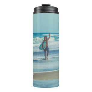 Man carrying surfboard at beach thermal tumbler