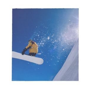 Man flying through the air on a snowboard with notepad