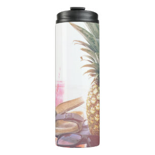 Minimalist photography of pineapple near sandals a thermal tumbler