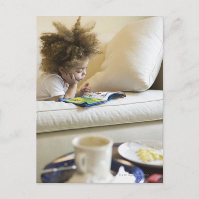 Mixed race boy reading book on sofa postcard (Front)