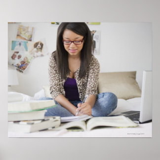 Mixed race teenage girl doing homework on bed poster