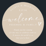 Modern Beige / Tan Wedding Welcome Hotel Bag Classic Round Sticker<br><div class="desc">Dark Tan / Beige Hotel Bag Stickers: Create a natural, modern look with these beige wedding welcome stickers. Each 3-inch round label features “welcome friends & family” in graceful handwriting with a heart accent and your personalised names and wedding date. The rich tan background and clean white script offer a...</div>