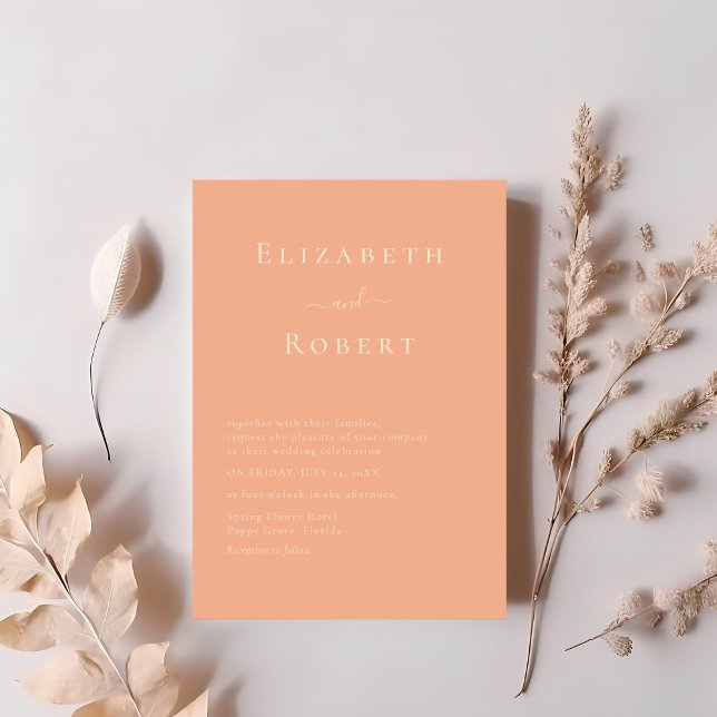 Modern Chic Coral Peach Minimalist Script Wedding Invitation (Modern Chic Coral Peach Minimalist Script Wedding Invitation on a table next to soft pink flowers)