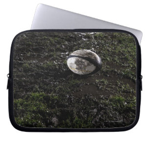 Muddy rugby ball sitting on a chewed up grass laptop sleeve