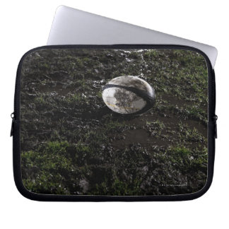 Muddy rugby ball sitting on a chewed up grass laptop sleeve
