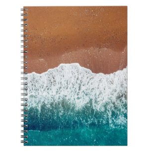 Ocean wave on a sandy beach, background top view notebook