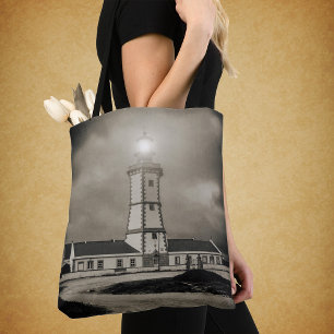 Old lighthouse on a storm night tote bag