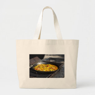 Paella is cooked on a grill large tote bag
