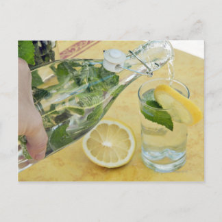 Person pouring water (mint-filled) into a glass postcard