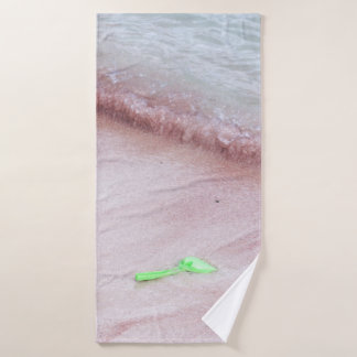 Person's foot beside green shovel on seashore bath towel