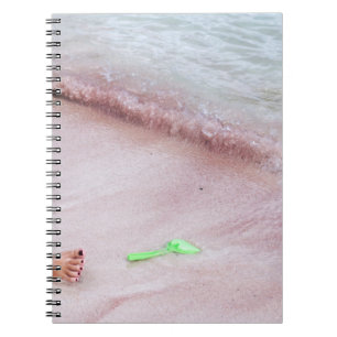 Person's foot beside green shovel on seashore notebook