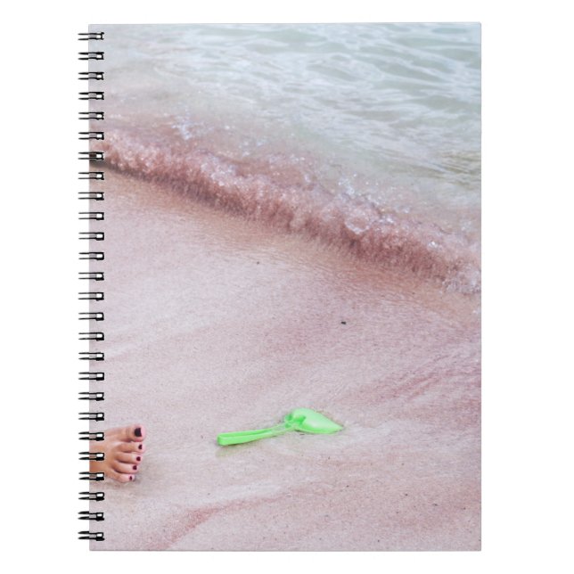 Person's foot beside green shovel on seashore notebook (Front)