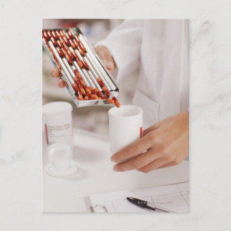 Pharmacist in drug store measuring pills into postcard
