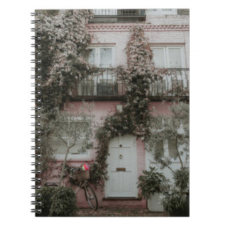 PINK AND WHITE PAINTED HOUSE COVERED WITH PLANTS A NOTEBOOK
