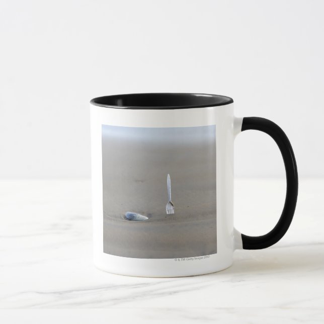 plastic fork sticking in sandy beach beside mug (Right)