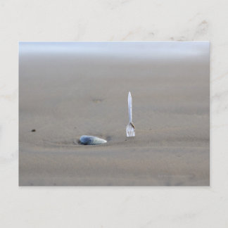 plastic fork sticking in sandy beach beside postcard