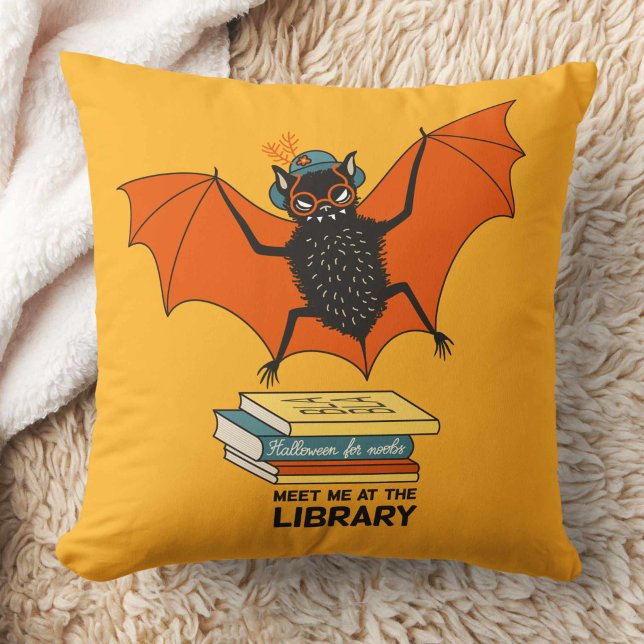 Reading Bat | Whimsical Librarian with Books Cushion (yellow pillow with a cute cartoon bat with eyeglasses and hat flying over some books)