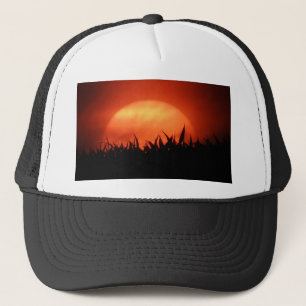 Red sundown behind black grass trucker hat