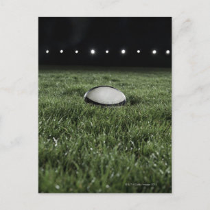 Rugby ball sitting on the grass pitch of a postcard